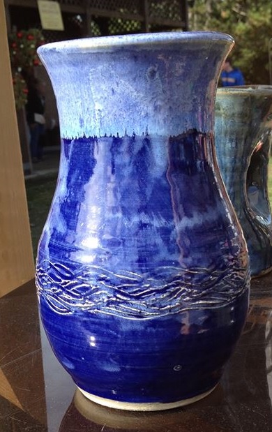 A clay pot with light blue painted on the top and dark blue painted from the middle to the bottom. There is a woven design etched into the bottom area of the pot